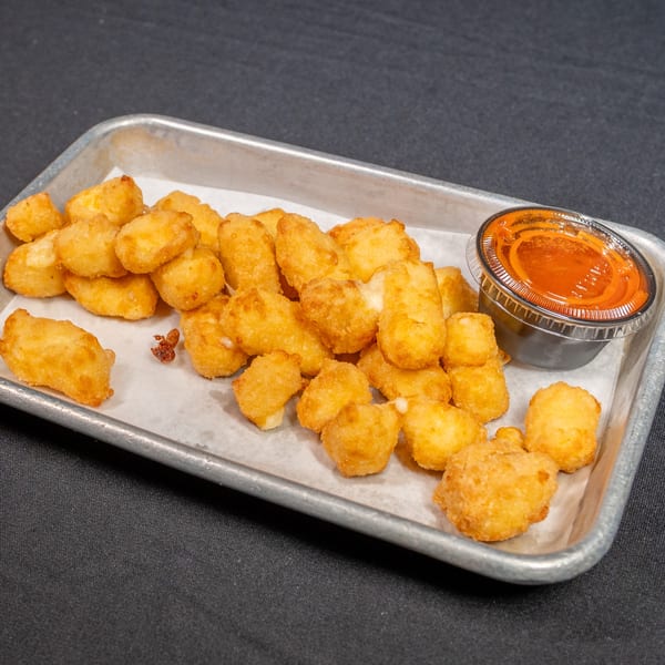 Golden fried cheese curds and a side of hot sauce on a metal tray from The Luverne Chicken Shack.